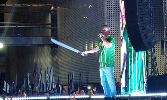 Flávio Bolsonaro com espada de plástico que lhe foi entregue por alguém da plateia (Foto: Lucas Arruda/CBN)
